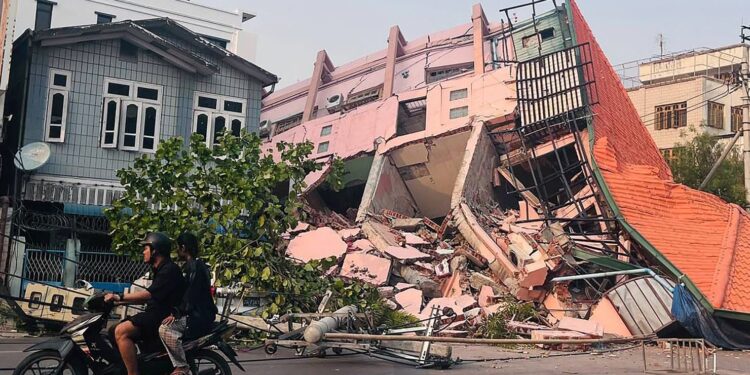 People drive on a motorbike past a collapsed building in Mandalay on March 28, 2025, after an earthquake in central Myanmar. Stringer/AFP/Getty Images