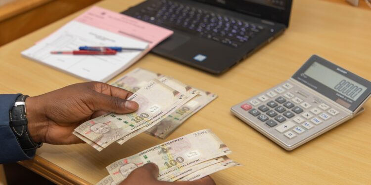 Photo of a hand holding Emalangeni banknotes with a calculator in the background,