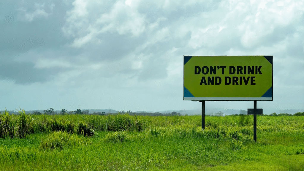 Don't Drink And Drive warning sign on side of a rural highway beside a sugar cane field