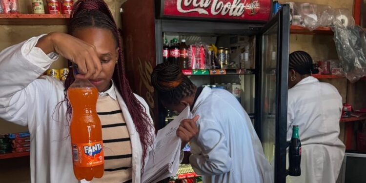 Health inspectors examine the expiry date on a bottled drink during a joint operation in Msunduza, while other officials inspect shelf items for compliance in the background. Photo: Municipal Council Of Mbabane