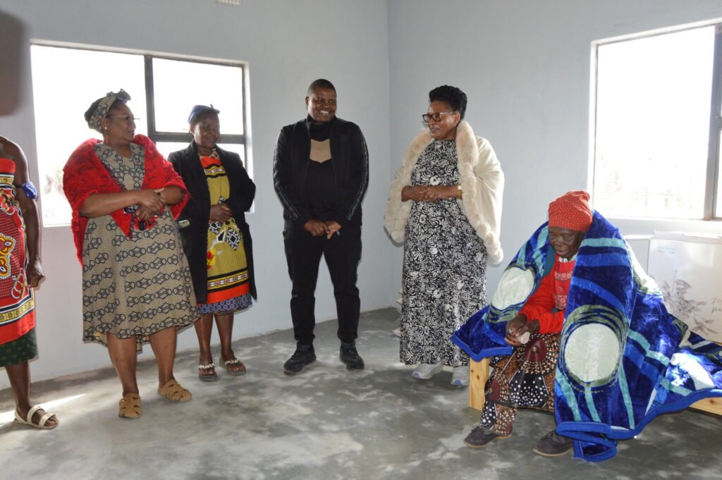 Deputy Prime Minister Thulisile Dladla shares a moment with Gogo Fakubi Mkhabela inside her new home, surrounded by family and community members.
