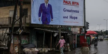 Robert, 75, carries bread to resell as he walks past an election campaign billboard for Cameroon’s 92-year-old President Paul Biya, who is seeking an eighth term in a presidential election scheduled on October 12, in Douala, Cameroon, on October 4, 2025 [Zohra Bensemra/Reuters]