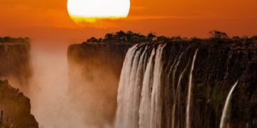 Victoria Falls cascading into the Zambezi Gorge as seen from Zimbabwe’s side, with mist rising and rainbows forming in the spray.