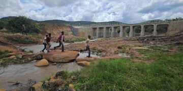 Children make their way across the river using rocks while the newly commissioned Dlomodlomo Low Level Crossing stands in the background. Photo by Microprojects MEPD.