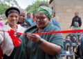 Deputy Prime Minister Thulisile Dladla cuts the ribbon during the official handover of a newly built one room house to 72 year old storm survivor Mkhulu Mbulawa Sigugudla Dlamini in the Lubombo region. Photo credit DPMO.