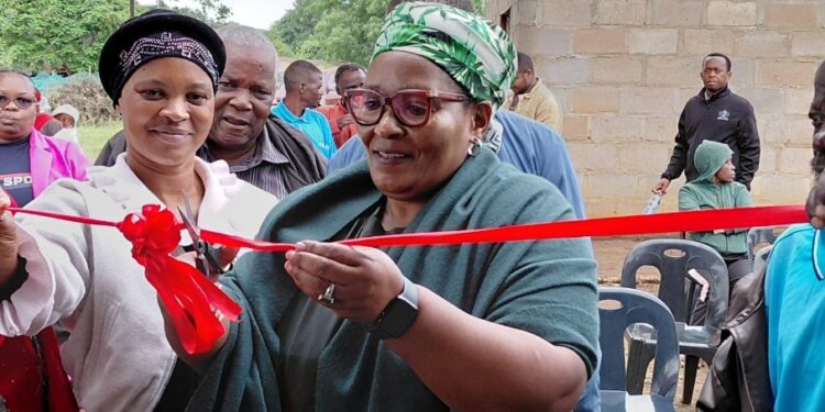 Deputy Prime Minister Thulisile Dladla cuts the ribbon during the official handover of a newly built one room house to 72 year old storm survivor Mkhulu Mbulawa Sigugudla Dlamini in the Lubombo region. Photo credit DPMO.