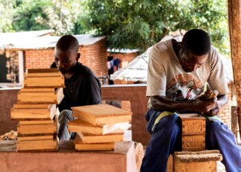 Two traditional wood sculptors at work, shaping carved figures. Photo by UNESCO.