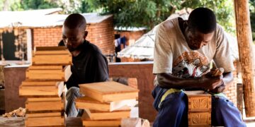 Two traditional wood sculptors at work, shaping carved figures. Photo by UNESCO.